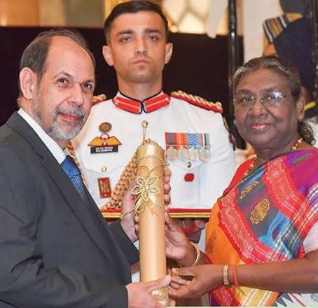Hormusji N. Cama, in a dark suit, receives the Padma Bhushan citation from President Droupadi Murmu at Rashtrapati Bhavan; an aide-de-camp in ceremonial uniform stands between them.